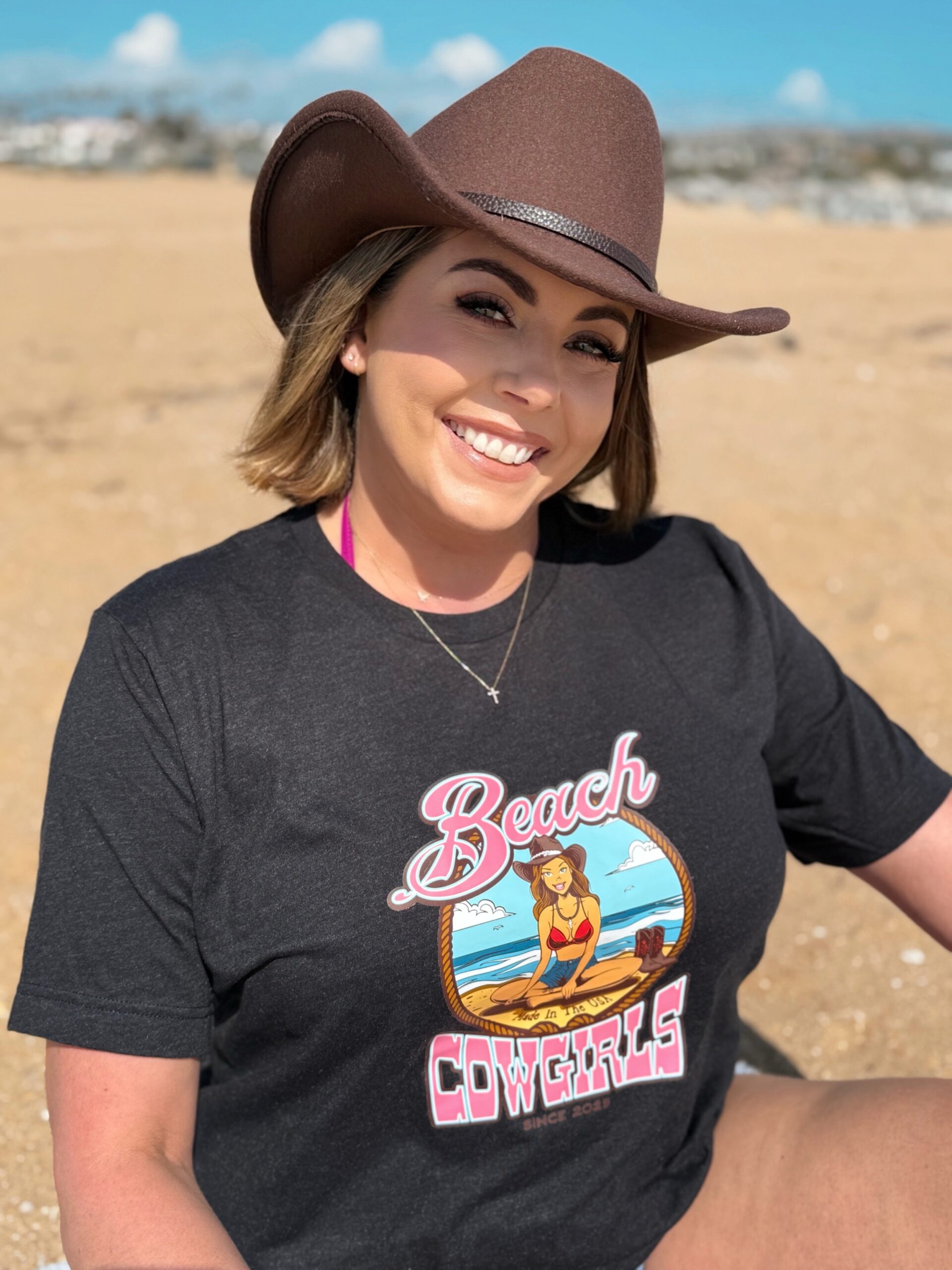 Stacy Head shot A woman sitting on the beach wearing a cowboy hat.